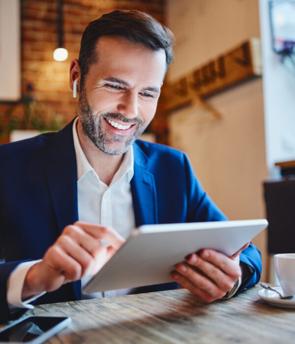 Businessman sitting in cafe looking at tablet during phone call through wireless headphones